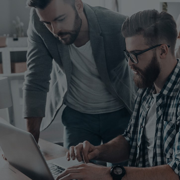 A photograph of two men huddled around a laptop